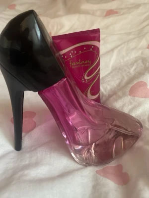 Parfymflaska formad som högklackad sko/britney Spears body lotion  - Unik parfymflaska i form av en högklackad sko med svart klack och rosa glas. Flaskan har en modern och trendig design som sticker ut på sminkbordet. Perfekt för dig som gillar snygga detaljer och vill ha något annorlunda i din parfymkollektion.
