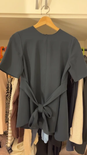 Mörkblå topp med knyt från Zara Woman - Snygg mörkblå topp från Zara Woman med korta ärmar och ett brett knytband i midjan som ger en fin siluett. Toppen har rund halsringning och är tillverkad i ett mjukt, lätt material som känns bekvämt mot huden.