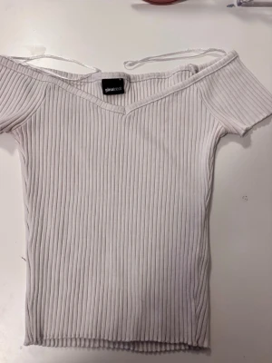2 Ribbade offshoulder-toppar Gina Tricot - Två ribbade offshoulder-toppar från Gina Tricot i svart och ljusbeige. Båda har kort ärm, v-ringning och smala axelband. Perfekta att styla med jeans eller kjol för en trendig look.