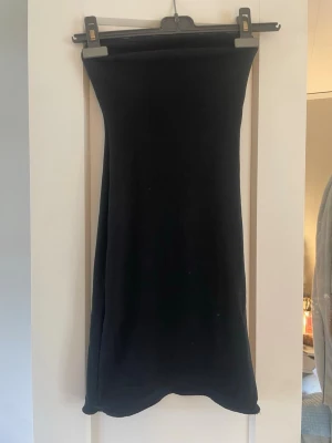 Svart tubklänning från Zara - Säljer en svart, enkel tubklänning från Zara. Klänningen är axelbandslös och har en tight passform som framhäver figuren. Perfekt att styla med smycken eller en cool jacka. Materialet känns mjukt och stretchigt, troligen bomull eller syntet.
