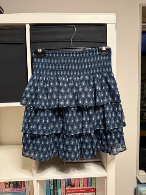 Blå volangkjol från Lindex - Supersöt blå kortkjol från Lindex med volanger och elastisk midja. Har använt få gånger. Går även att ha som tubtopp!