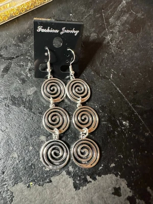 Silvriga spiralörhängen i metall - Säljer ett par statementörhängen i silverfärgad metall med tre stora spiralformade hängen på varje örhänge. De har en cool och unik design som verkligen drar blickarna till sig. Perfekta för dig som gillar att sticka ut med dina accessoarer.