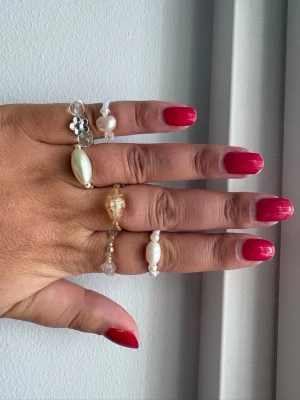 6st handgjorda ringar  - Säljer ett set med fyra handgjorda ringar i pärlor och kristaller. Ringarna har detaljer som silverfärgad blomma, vita och genomskinliga pärlor samt en större guldfärgad kristall. Perfekt för dig som gillar unika accessoarer och vill mixa olika stilar. Storlek 17-18 