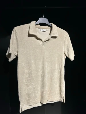 Beige frottépiké med krage - Säljer en beige piké i mjuk frotté med klassisk krage och korta ärmar. Perfekt för en avslappnad och chill stil. Skjortan har en enkel design utan synliga knappar och är riktigt skön att bära.   Strlk 146/152
