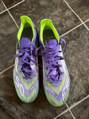 Lila Adidas F50 PRO fotbollsskor - Säljer ett par Adidas F50 fotbollsskor i lila och neongult med vita detaljer. Skorna har snörning, låg profil och mönstrad ovandel i syntetmaterial. Perfekta för dig som vill sticka ut på planen med både stil och funktion.  