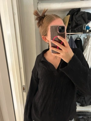 Svart ribbad tröja med krage - Säljer en svart långärmad tröja med krage och ribbad struktur. Tröjan har en avslappnad passform och mjukt material som känns skönt mot huden. Perfekt för dig som gillar en enkel men stilren look.