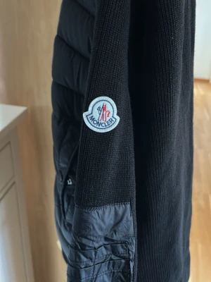 Moncler cardigan - Moncler Cardigan  Svart Moncler cardigan i mycket fint skick. Säljes då den tyvärr var lite för liten för mig och därför inte kommer till användning.  -Mycket fint skick -Stilren och lätt att matcha -Aldrig använd då den var för liten, endast testat ha den på mig. -Storlek: Medium  Skicka ett meddelande vid intresse eller om du vill ha fler bilder/mått. Seriösa köpare välkomna!