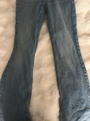 Ljusblå bootcut jeans - Säljer ett par ljusblå bootcut jeans med klassisk femficksdesign och normalhög midja. Jeansen har en lätt tvättad look och raka ben som går ut något nedtill. Perfekta till sneakers eller boots för en avslappnad stil.