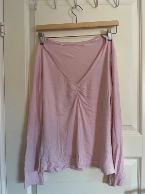 Ljusrosa långärmad v-ringad topp - Ljusrosa långärmad topp med djup v-ringning. Tillverkad i ett tunt, mjukt material. Den är i väldigt bra skick, inte kommit till användning 