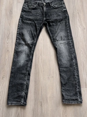 Svarta tvättade raka jeans - Säljer ett par svarta jeans med tvättad look och raka ben. Jeansen har klassisk femficksmodell och normal midja. Materialet är denim med snygga slitningar för en avslappnad stil. Perfekta till sneakers eller boots. Den passar även till dom som har 30/30 