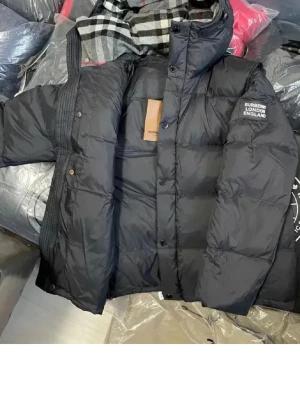 Svart dunjacka från Burberry - Säljer en svart dunjacka från Burberry med huva och klassiskt rutigt foder. Jackan har tryckknappar, dragkedja och logotyp på ärmen. Perfekt för kalla vinterdagar och riktigt snygg till streetwear-stilen.