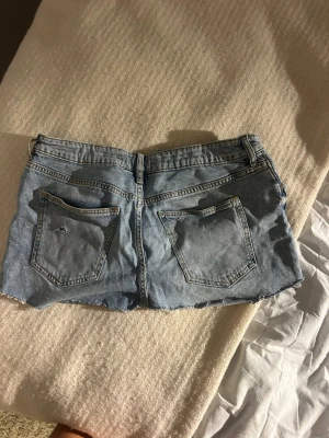 Ljusblå jeanskjol - Kort jeanskjol i ljusblå denim och slitningar framtill. Kjolen har klassiska fem fickor och knappgylf. Perfekt för en avslappnad och trendig look. Avklippta jeans 💓