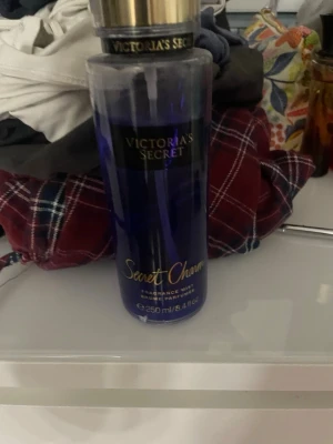 Victoria's Secret Secret Charm mist - En parfymmist från Victoria's Secret i doften Secret Charm. Flaskan är genomskinlig med blått och guldiga detaljer samt guldfärgat lock. Volymen är 250 ml och flaskan har en elegant, cylinderformad design.