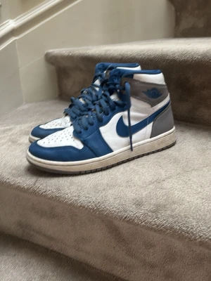 Nike Air blåvita sneakers - Snygga Nike Air sneakers i blått och vitt med klassisk design. Skorna har blå snörning, vit tåbox med perforeringar och blå detaljer runt om. Tillverkade i läder och textil för en stilren look som passar till det mesta.