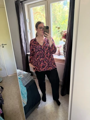 Blommig blus med v-ringning - Mönstrad blus i vinrött och rosa med blommor och v-ringning. Blusen har lång ärm och lös passform som ger en avslappnad look. Materialet ser ut att vara mjukt och lätt, perfekt för en trendig vardagsstil. Från märket Odd Molly i storlek 5 som enligt deras storlekguide motsvarar en storlek XXL. Helt ny med tags/ prislapp fortfarande kvar. 