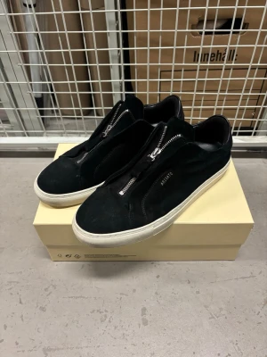 Axel Arigato Clean 90 Zip  - Axel Arigato Clean 90 Zip – Black Suede – Stl 44  Säljer ett par Axel Arigato Clean 90 Zip i svart mocka.  En stilren modell med silverfärgade dragkedjor framtill, vit sula och diskret Axel Arigato-logga på sidan.  Modell: Clean 90 Zip Storlek: EU 44 / US 10.5 / UK 9.5 Färg: Black Material: Mocka Skick: Begagnade i bra skick med normalt bruksslitage. Sulorna har mindre smuts/märken, se bilder för aktuellt skick. Tillbehör: Original Axel Arigato-skokartong medföljer.