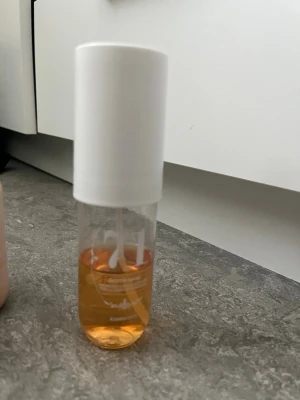 Aromaspray nr 71 med vit kork - Transparent parfymflaska med vit kork och orangefärgad vätska. Flaskan har tryckt text och siffran 71 på framsidan. Enkel och stilren design som passar perfekt i väskan eller på sminkbordet.