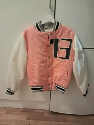 Rosa och vit bomberjacka Starter - En Snygg oanvänd archive unisex Ance Studio x Starter bomber/college jacket med svart/vita ribbade muddar och stor svart '13' på bröstet i Xxs/xs. Köp priset ligger på runt 5,1k. Står "Acne Studio Blå Konst Floragatan 13" på rygget. Längd: cirka 61 cm. Axelbred: cirka 42 cm. Perfekt för en trendig outfit.