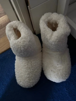Vita fluffiga tofflor från Kappahl - Supermysiga vita tofflor från Kappahl i storlek 38/39. De är gjorda i ett fluffigt, mjukt teddy-material som håller fötterna varma. Perfekta att glida runt i hemma när det är kallt ute. Hög modell som täcker ankeln för extra värme.