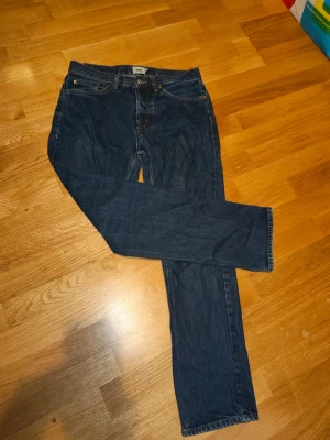 Mörkblå raka jeans - Säljer ett par mörkblå jeans med rak passform och klassisk femficksdesign. Jeansen har normal midja och stängs med dragkedja och knapp. Materialet är denim i bomull och de har en tidlös look som passar till det mesta.