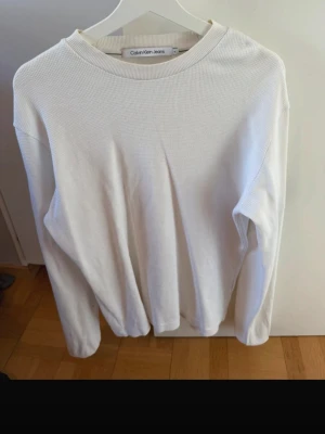 Vit stickad tröja Calvin Klein Jeans - Vit stickad tröja från Calvin Klein Jeans med rund halsringning och diskret struktur i materialet. Tröjan har långa ärmar och en klassisk passform. Perfekt för dig som gillar stilrena och enkla plagg.