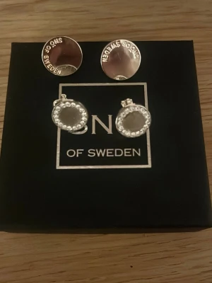 Clips örhängen från SNÖ of Sweden - Säljer två par clips örhängen från SNÖ of Sweden. Ena paret är runda silvriga studs med logotypen ingraverad, det andra paret är cirkelformade örhängen dekorerade med små vita pärlor runt kanten. Båda för 100 kr ett par för 50 kr💞
