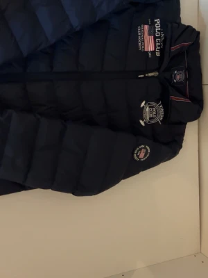 Höst jacka Vinson Polo Club - Snygg mörkblå dunjacka/lättviktsjacka från Vinson Polo Club i storlek 16 (passar ca 160–164 cl eller en slimmad XS). Jackan har märkestryck och patchar på bröstet, ärmen samt ryggen och passar perfekt för vår, höst eller svalare sommarkvällar. Om ni vill ha bild på tvättlappen kan jag leta på den för den är bortklippt😊