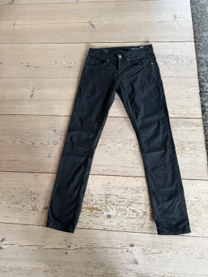 Svarta slim fit jeans, storlek 30 - Säljer ett par svarta slim fit jeans med klassisk femficksdesign och knappgylf. Jeansen har smal passform och raka ben, perfekta till en avslappnad men ändå stilren look. Materialet känns mjukt och följsamt, vilket gör dem sköna att bära hela dagen.
