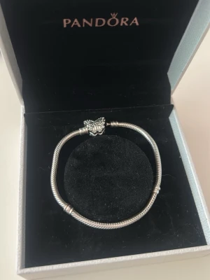 Pandora silverarmband med fjäril - Armband: Säljer ett stilrent silverfärgat armband från Pandora med en detaljerad fjärilsberlock. Armbandet har en klassisk orm-länk och kommer i originalask. Perfekt för dig som gillar att mixa och matcha med olika berlocker.    Berlockerna och avdelaren har 925 stämpel och är inköpta på Pandoras egna hemsida. Köps som ett paket för 1,000kr eller 499kr för armbandet och 199kr per berlock/avdelare.