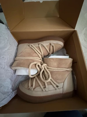 Beige moon boots från Inuikii - Säljer ett par snygga beige inukii boots från Inuikii med grov sula och rejäla snören runt hela skon. Bootsens ovandel är i mocka och läder, och de har en varm, trendig look som passar perfekt till vintern. Supersköna och stilrena för kalla dagar.