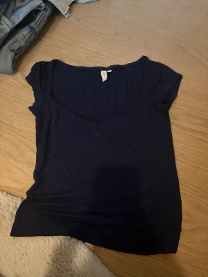 Mörkblå topp med spets från Nelly - Snygg mörkblå topp från Nelly med v-ringning och fina spetsdetaljer längs halsringningen. Kortärmad och i mjukt material som sitter skönt på kroppen. Perfekt att matcha med jeans eller kjol. Knappt använd