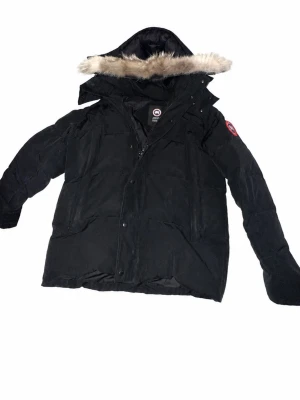 Canada Goose ”WYNDHAM”  - Säljer en svart dunjacka från Canada Goose med stor huva och fluffig pälsdetalj. Jackan har flera fickor framtill och klassisk Canada Goose-logga på ärmen. Perfekt för kalla vinterdagar och riktigt varm tack vare dunfyllningen, ända negativa e dragkedjan, den e lite trög men de är knappt ett problem. Scan finns, fin päls som inte känns eller ser fejk ut, kom pm för mer bilder och om ni vill se scan-taggen! OBS Pris diskuteras