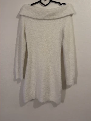 Vit offshoulder klänning - Mysig vit kortklänning med fluffig textur och offshoulder-design. Klänningen har lång ärm och är perfekt för dig som vill ha en stilren men ändå unik look. Passar till många olika tillfällen och är superbekväm tack vare det mjuka materialet.