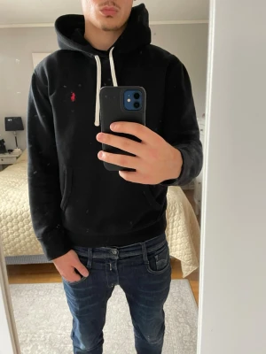Ralph Lauren Hoodie - Snygg svart hoodie från Polo Ralph Lauren med klassisk röd broderad logga på bröstet. Hoodien har vit dragsko i huvan och en stor magficka framtill. Tillverkad i mjukt material och har ribbade muddar vid ärmar och nederkant.