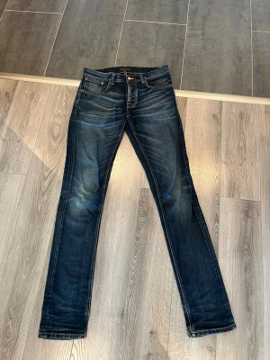 Nudie Jeans Grim Tim 32/34 - Säljer ett par riktigt snygga Nudie Jeans GrimTim i storlek 32/34! Mörkblå tvätt med snygga slitningar som är en del av designen. Jeansen ar använda men fortfarande i bra skick och passar perfekt till både sneakers och boots.  Först till kvarn! Skickas snabbt vid köp. Skriv gärna vid frågor eller bud.