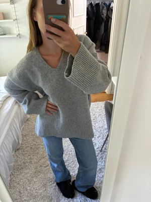 Oversized grå stickad tröja - Mysig oversized stickad tröja i ljusgrått med v-ringning och breda ribbade muddar vid ärmslut och nederkant. Tröjan har en avslappnad passform och är perfekt att bära till jeans eller leggings. Materialet känns mjukt och värmande. Perfekt nu till hösten 