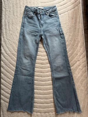 Ljusblå flare jeans från MNG - Snygga ljusblå flare jeans från MNG med råa kanter nertill och klassisk femficksdesign. Jeansen har hög midja och utsvängda ben, perfekt för en trendig och avslappnad look. Tillverkade i mjuk denim med dragkedja och knapp framtill.
