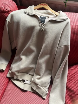Beige halfzip hoodie från Bershka - Säljer en beige hoodie från Bershka i storlek XS. Hoodien har en halv dragkedja med ringdetalj, ribbade muddar och mjukt fleecefoder på insidan. Perfekt för chill dagar och enkel att matcha med jeans eller mjukisbyxor.