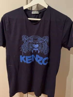 Mörkblå Kenzo t-shirt med tigertryck - Snygg mörkblå t-shirt från Kenzo med ikoniskt blått tigerbroderi och logga på bröstet. Klassisk passform och rund halsringning. Perfekt för dig som vill sticka ut med en trendig och stilren look.