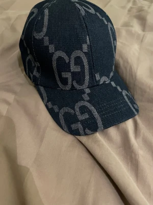 Mörkblå keps Gucci - Snygg mörkblå keps i denim-look med stort GG-mönster i grått över hela kepsen. Klassisk böjd skärm och sexpanelers design. Perfekt accessoar för att lyfta din streetwear-stil.
