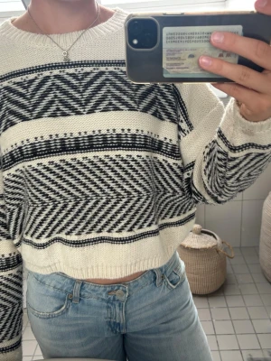 Vit och svart mönstrad stickad tröja - Säljer en oversized stickad tröja i vitt med svarta grafiska mönster. Tröjan har rund halsringning, långa ärmar och ribbade muddar. Materialet är mjukt och tjockt, perfekt för kyligare dagar. Passar till jeans eller kjol för en avslappnad look. 