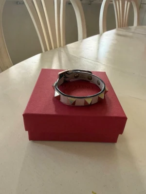 Valentino ljusrosa läderarmband - Säljer ett snyggt ljusrosa armband från Valentino i äkta läder. Armbandet har guldiga pyramidformade nitar runt om och ett justerbart spänne. Perfekt accessoar för att lyfta din outfit med en edgy touch.