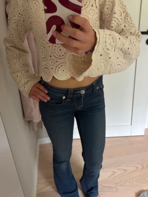 Blå low waist True Religion jeans bootcut - Säljer ett par blå jeans från True Religion med klassisk kontrastsöm och ikonisk fickdesign bak. Modellen har bootcut med låg midja