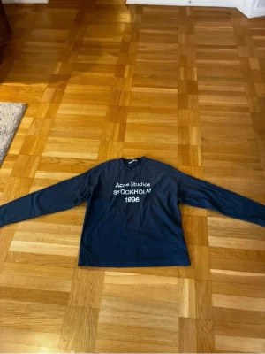 Mörkblå långärmad Acne Studios tröja - Snygg mörkblå långärmad tröja från Acne Studios med vit text 'STOCKHOLM 1996' på bröstet. Klassisk rak passform och rund halsringning. Perfekt för dig som gillar stilrena och trendiga plagg med enkel design.