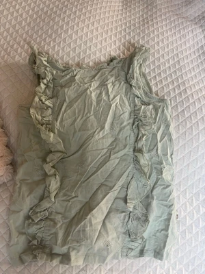 Ljusgrön volangtopp från Pimkie - Supersöt ljusgrön topp från Pimkie med volangdetaljer längs axelbanden och framtill. Ärmlös modell i tunt, mjukt tyg med små broderade detaljer. Perfekt för en fräsch och somrig look.