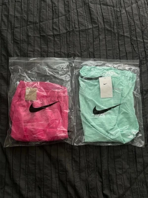 Nike set - Helt ny, snyggt träningsset från Nike med en mintgrön t-shirt och knallrosa shorts. Båda plaggen har Nike-logga och är tillverkade i lätt, snabbtorkande material. Shortsen har resårmidja och dragsko för bästa passform. Perfekt för gymmet eller löprundan.