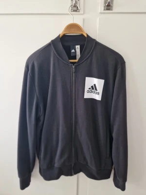 Svart bomberjacka från Adidas - adidas Träningströja Essentials Bomber - Svart  Använd men i fint skick skick  Storlek: M  Se mer info här: https://www.unisportstore.se/fotboll365/adidas-traningstroja-essentials-bomber-svart/157336/  Passar inte priset, ge ett rimligt bud.  Kika gärna på mina andra annonser, fyller på löpande då jag rensar hemma
