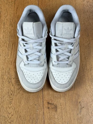 Adidas Forum Low CL | Vit/Grå | Storlek 42 | Gott skick - Klassiska Adidas Forum Low CL i vit/grå colorway med suede- och läderdetaljer.  Skick: Gott använt skick. Sparsamt använda – sulorna nästan oslitna. Midsolen är något gulnad (vanligt på äldre Forum, syns på bild). Litet hål i innerfodralet som inte syns utifrån – reparationslapp medföljer om önskat.