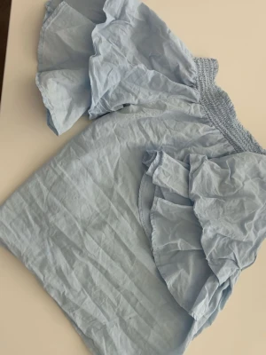 Ljusblå offshoulder blus med volang - Supersöt ljusblå offshoulder blus med bred smock upptill och stora volangärmar. Blusen är sååå fin men kommer inte till användning står tyvärr inte vart den är ifrån 