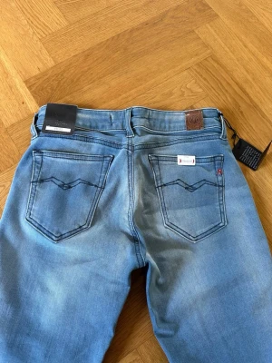 Ljusblå raka jeans från Replay - Säljer ett par ljusblå jeans från Replay med raka ben och klassiska bakfickor. Jeansen har en snygg tvättad look, detaljerade sömmar och Replay-lapp på bakfickan. Perfekta för en avslappnad och trendig stil. Low waist och helt nya!